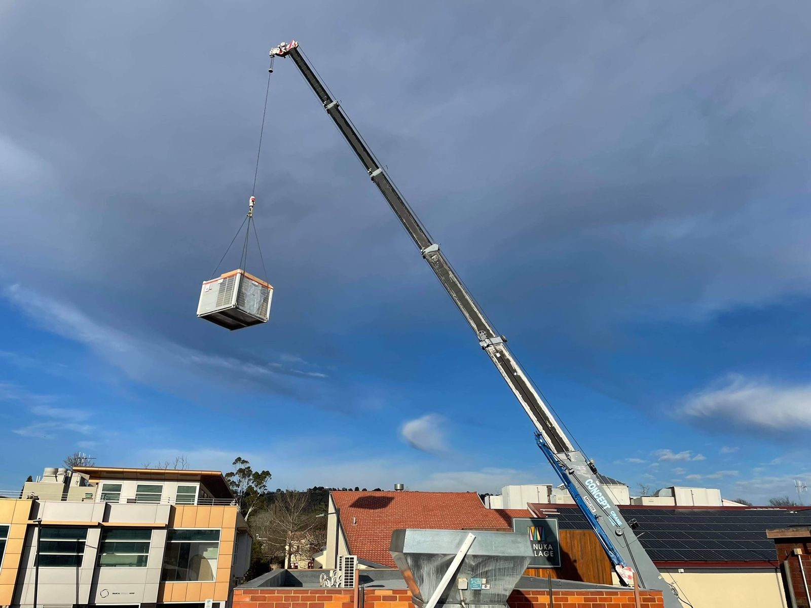 Crane lifting a commercial air conditioning unit onto a building roof