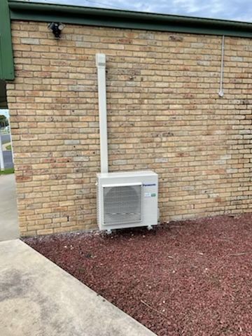 Outdoor air conditioner unit on gravel beside a brick wall